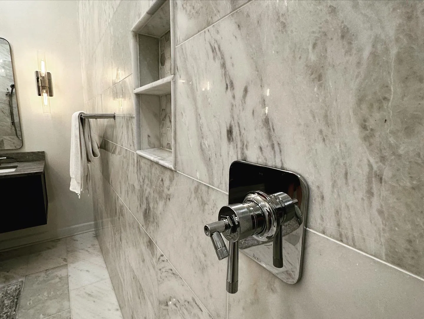 Close-up of marble shower tiling with a recessed niche and polished chrome valve