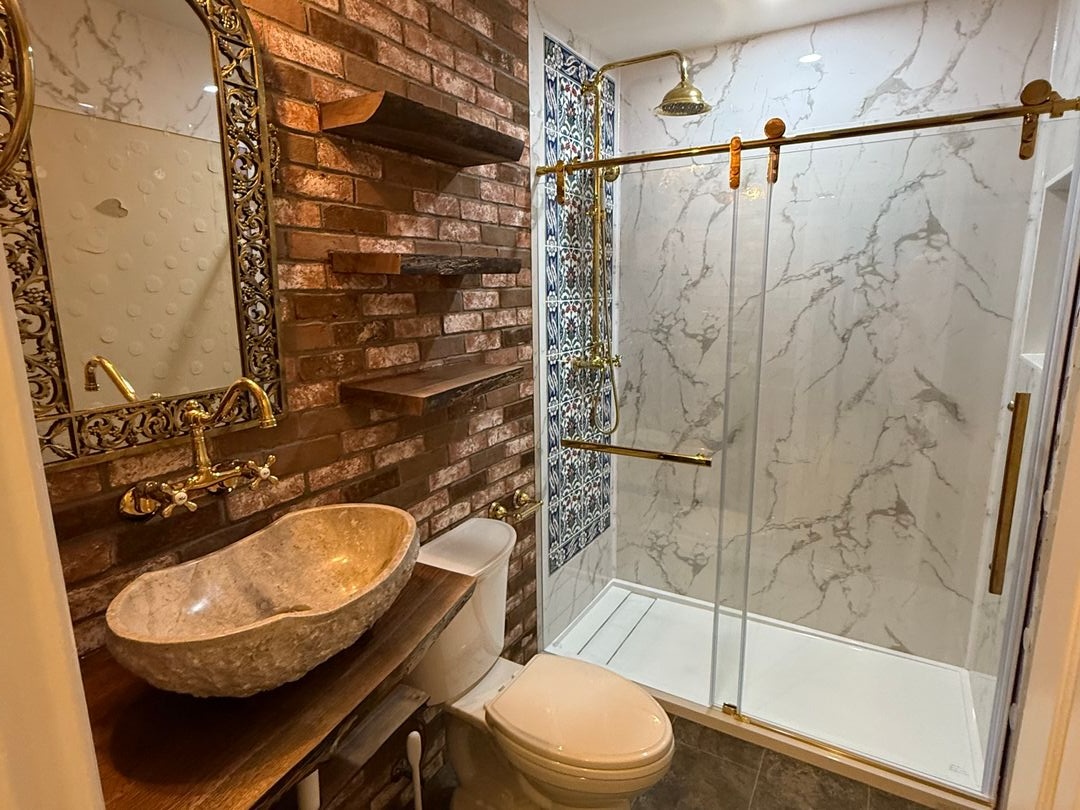 Bathroom remodel with an exposed brick wall, marble shower enclosure, brass fixtures and a carved stone vessel sink