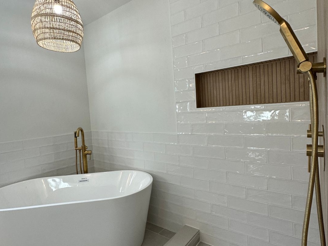 Bathroom remodel with a freestanding white tub, glossy handmade-look wall tile, brass fittings and a fluted wood shower niche
