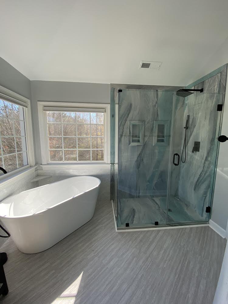 Primary bathroom remodel with a freestanding tub beneath a bay window and a glass corner shower in blue-grey marble